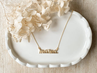 Gold 'mama' necklace on a white dish with beige flowers