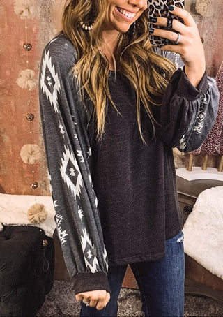 Woman taking a selfie in a patterned sweater and jeans with a decorative wall in the background.