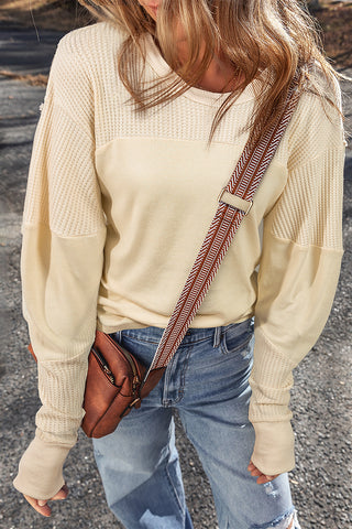 Person wearing a beige buttercup sweatshirt and blue jeans with a brown leather bag over the shoulder.