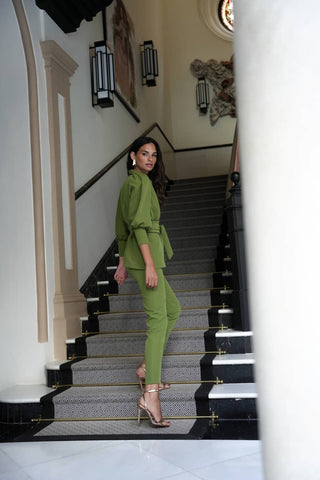 Woman in a green outfit standing on a staircase in an elegant interior setting